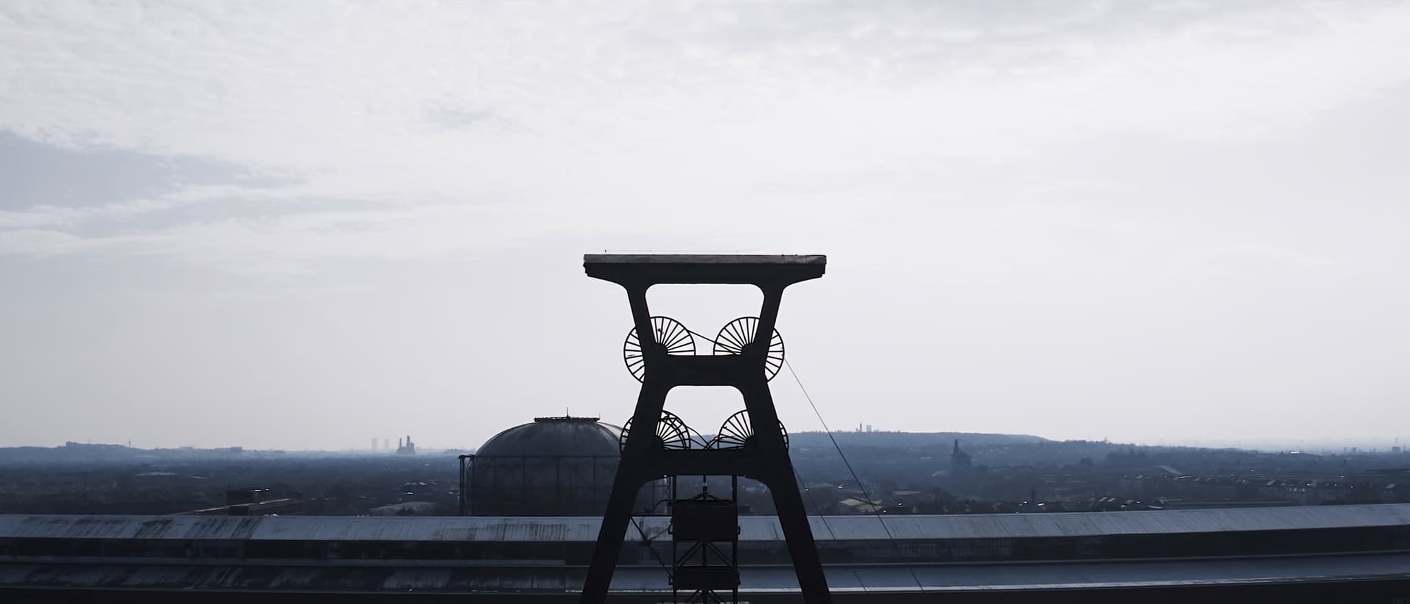 A pit headframe with two pulley wheels, a flat industrial horizon behind it
