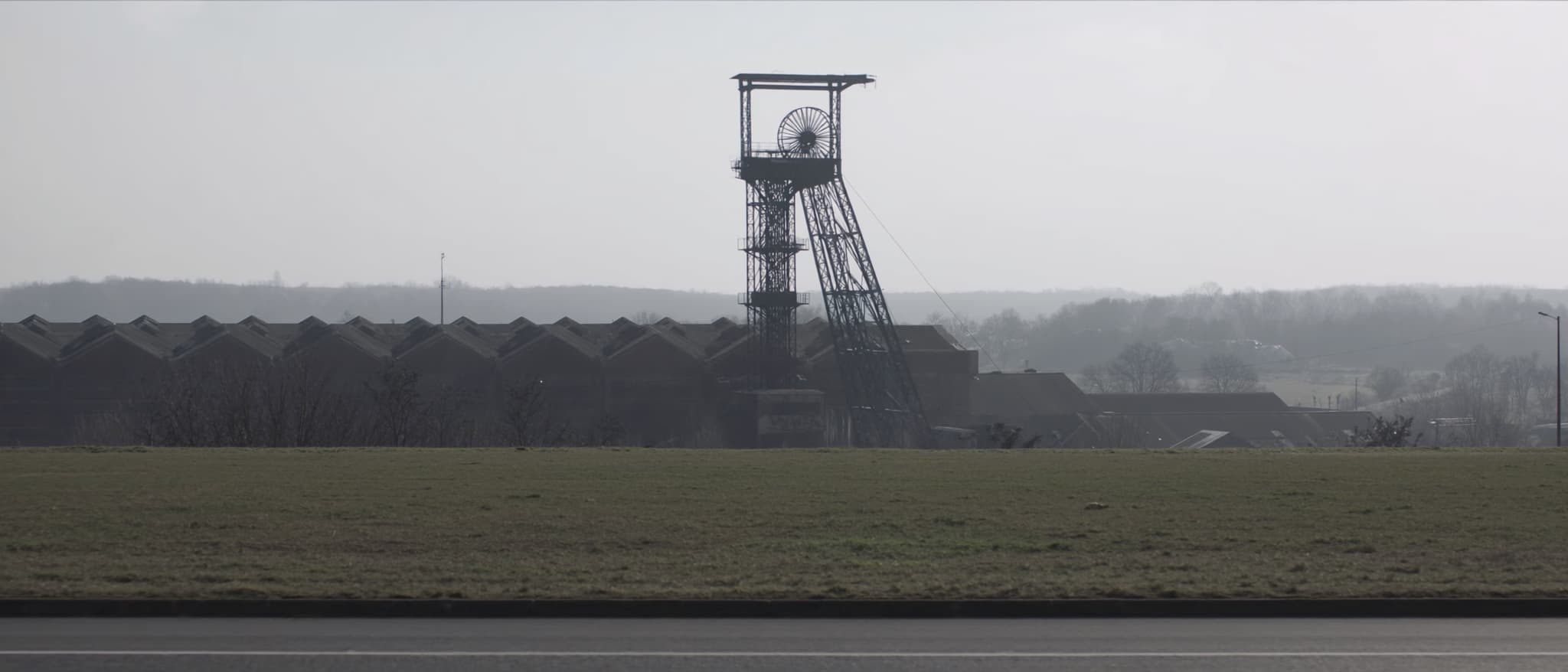A winding tower over the halls of a colliery, wide open ground in front of it