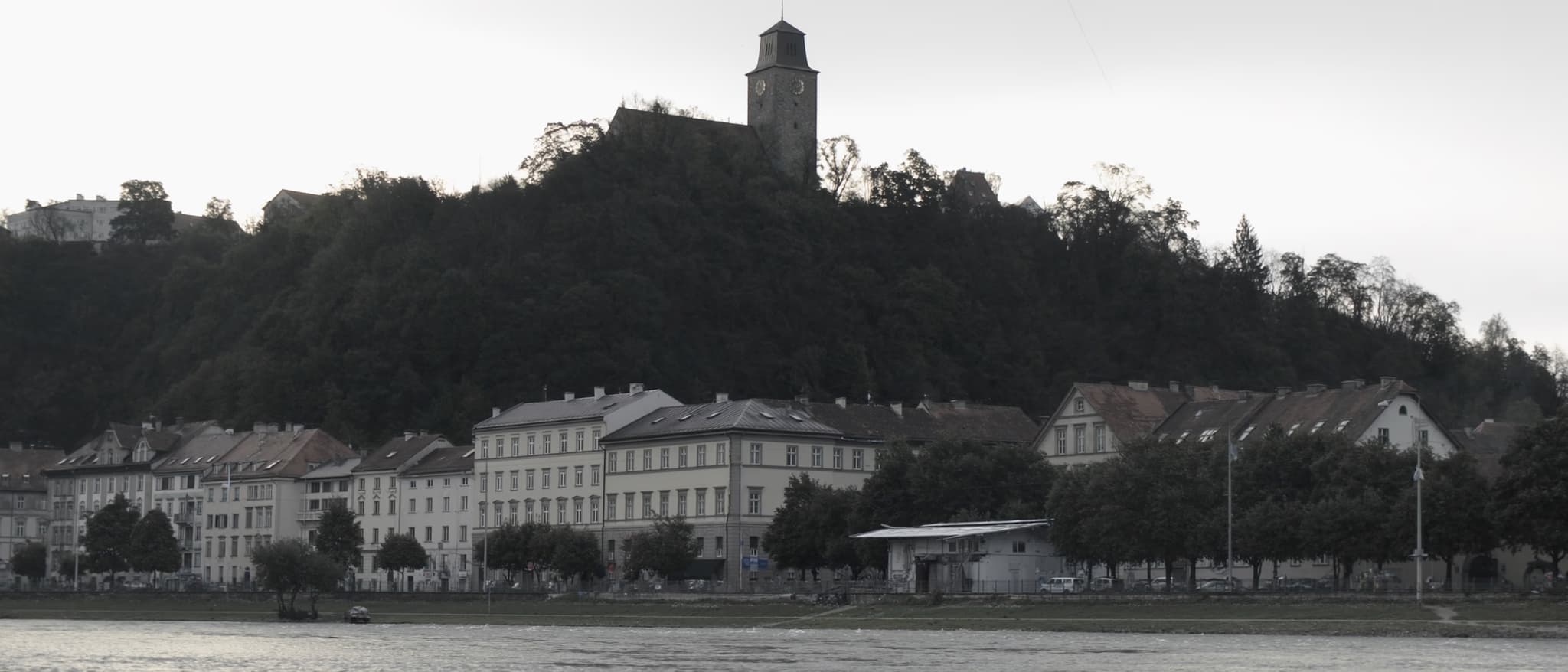 Reka, pošumljeno brdo nad krovovima, sat-kula na njemu