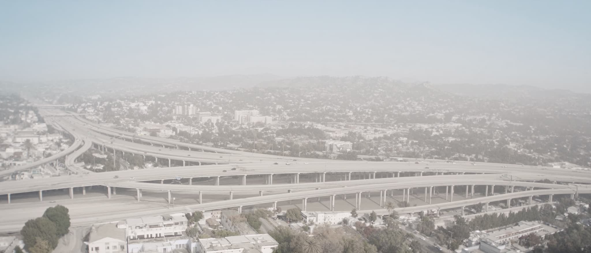A multi-level freeway interchange over the flat city, dry hills behind it