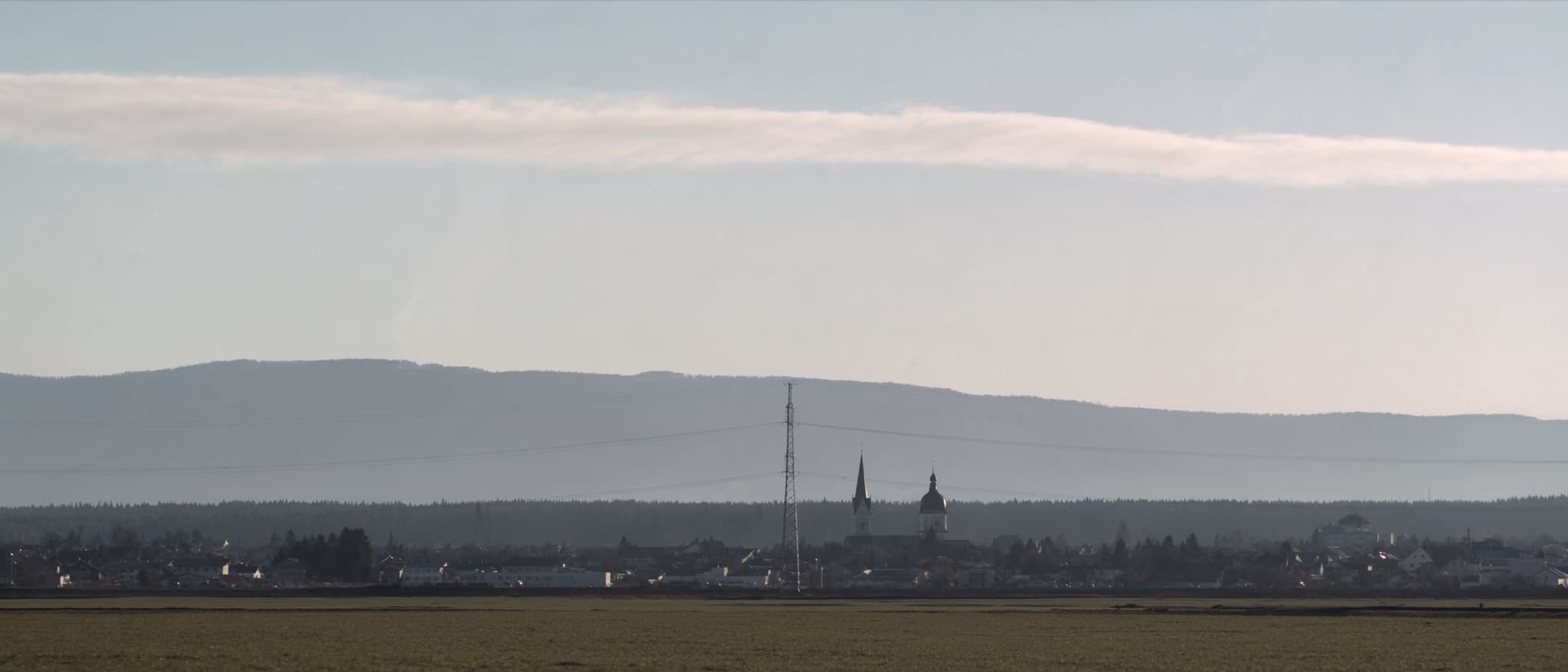 Flat land, a small town, and the chain of the Alpine foothills behind it