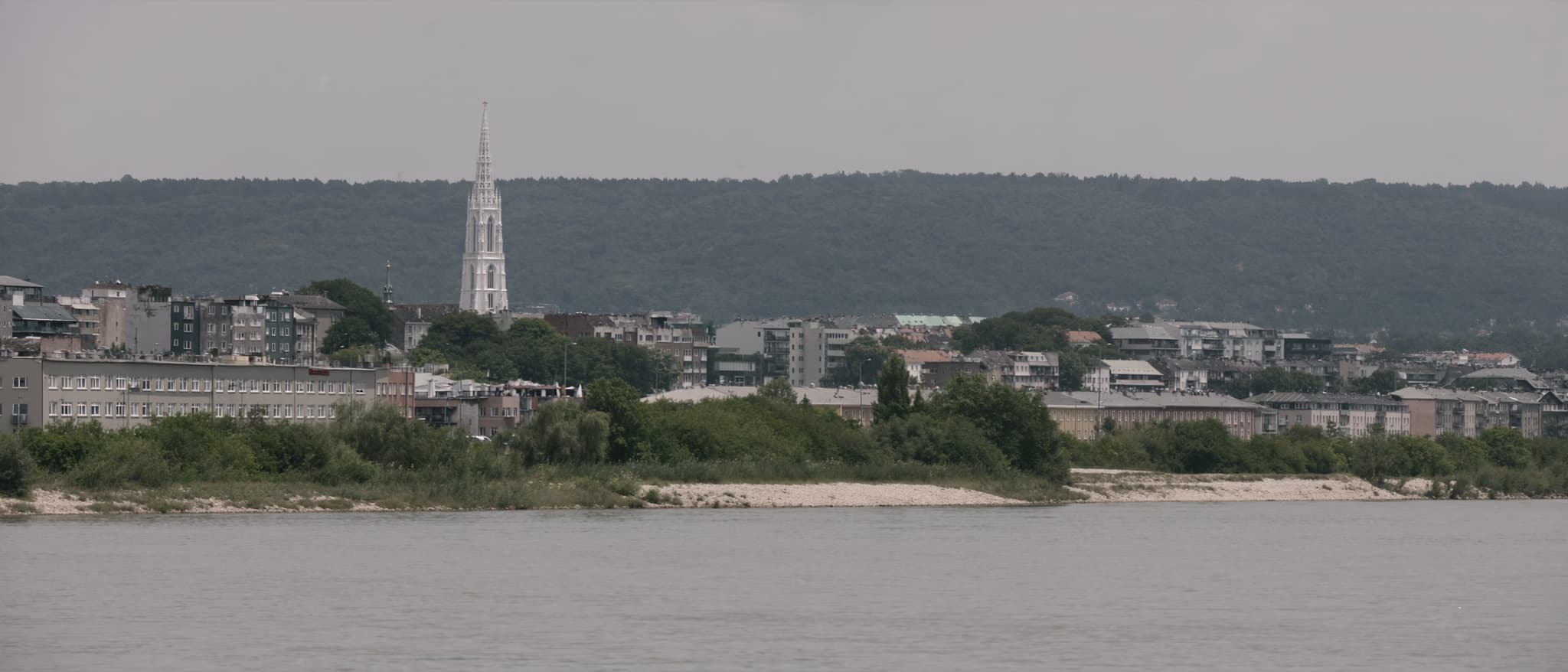 Reka, gotički toranj nad niskim gradom, pošumljeni greben iza njega